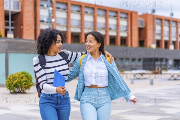 Happy multi-ethnic latin and chinese female students walking embraced along the university campus