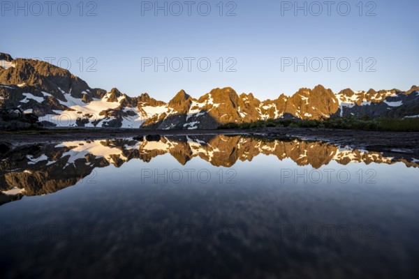 Rocky mountain peaks reflected in a small pond, mountain landscape with alpenglow at sunrise, at the Trollfjord Hytta, at the Trollfjord, Lofoten and Vesterålen, Nordland, Norway, Europe