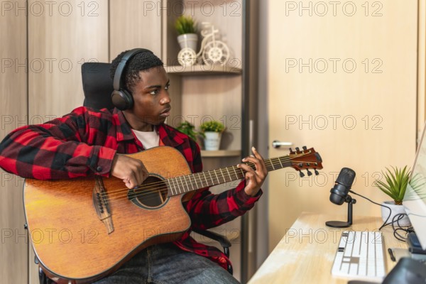 Concentrated young man playing the acoustic guitar in his home studio, composing a new song and recording with a microphone