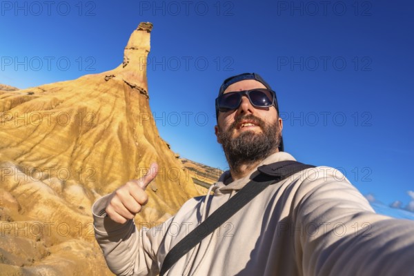 Tourist taking a selfie and gesturing thumbs up in front of a sandstone peak in bardenas reales desert, navarre, spain