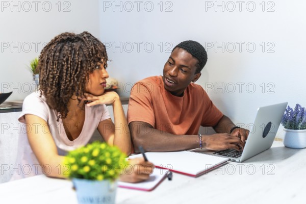 Young black couple collaborating on a laptop, taking notes and engaging in productive remote work from the comfort of their home office