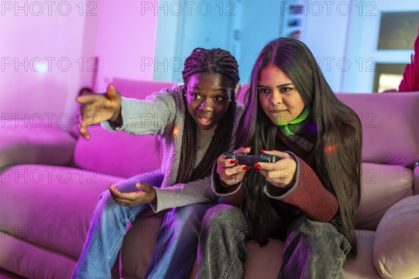Two focused female students enjoying a gaming session on a cozy sofa at home, sharing laughter and excitement during their leisure time