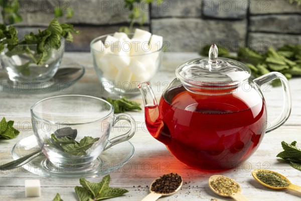 Touched teapot, glasses with mint, pieces of sugar and different types of tea on a table in front of a stone background
