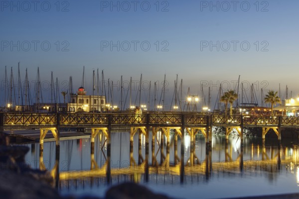 Evening atmosphere at the harbour with illuminated bridge and reflecting mast structures in the water, Playa Blanca, Lanzarote, Canary Islands, Spain, Europe