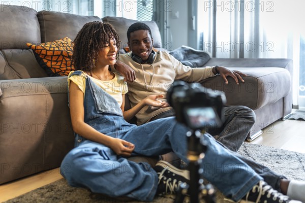 Two videomakers are creating content for their channel, discussing and smiling while recording a vlog in their living room