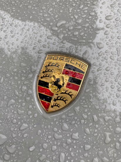 Porsche crest on grey bonnet of sports car with sparkling raindrops, international