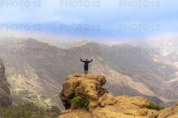 Hiker celebrating at the summit of roque nublo in gran canaria, soaking in stunning views of the volcanic landscape
