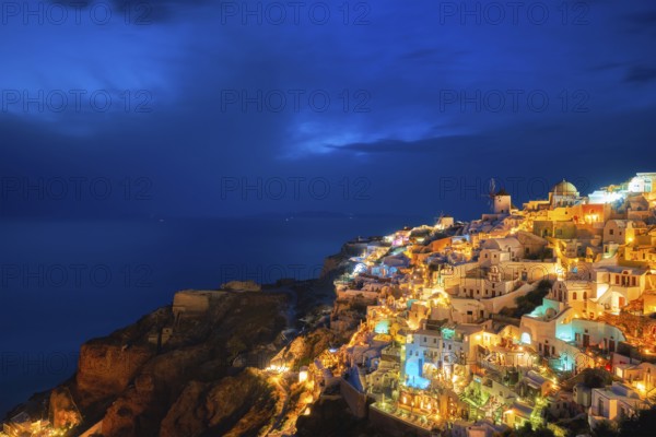 Famous greek iconic picturesque tourist destination Oia village with traditional white houses and windmills in Santorini island in the evening blue hour, Greece, Europe