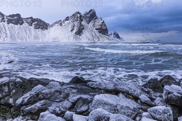 Iced rocks on the beach of Stokkness, behind them the snowy rocky slopes of Vestrahorn, near Höfn, Sudausturland, Iceland, Europe