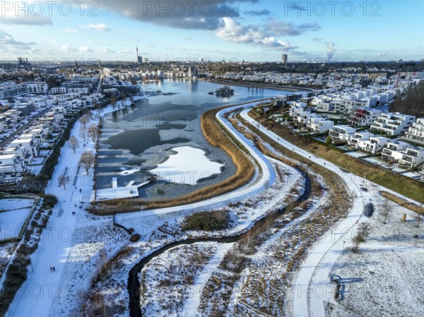 Dortmund, North Rhine-Westphalia, Germany, Phoenix Lake in winter with snow, renaturalised Emscher in front. The river was transformed into a near-natural body of water, flood protection and biodiversity through newly designed floodplains. A former industrial wasteland of 99 hectares was transformed into residential, work and leisure areas and 24 hectares of lake surface. In the event of heavy rainfall, the lake acts as a rainwater retention basin. Following the construction of a parallel sewer, the Emscher is now free of wastewater, having previously been an open, above-ground wastewater sewer, combined sewer with surface water and wastewater. The Phoenix Lake, a showcase project for structural change, is an artificial lake on the site of the former Phönix Ost steelworks in Dortmund's Hörde district, Europe
