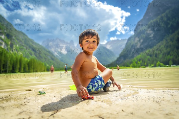 Smiling child playing with a toy car on the shore of lake landro, also called durrensee, in the italian dolomites, enjoying the summer holidays