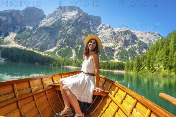 Young woman relaxing on a wooden rowboat at lake braies, enjoying the turquoise water and stunning dolomite landscape on a sunny day