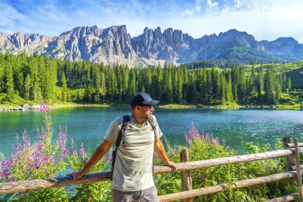 Hiker admiring the stunning landscape of lake carezza with the latemar mountain range in the background, dolomites, italy
