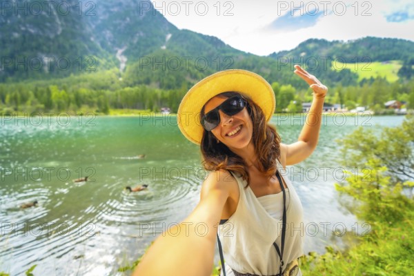 Happy tourist taking a selfie at lake dobbiaco with ducks swimming in the emerald green water and the dolomites in the background during summer holidays