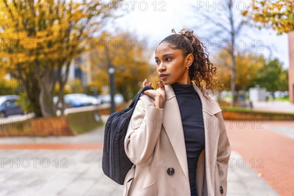 Elegant african american young businesswoman wearing trench coat carrying hand bag in the city in autumn