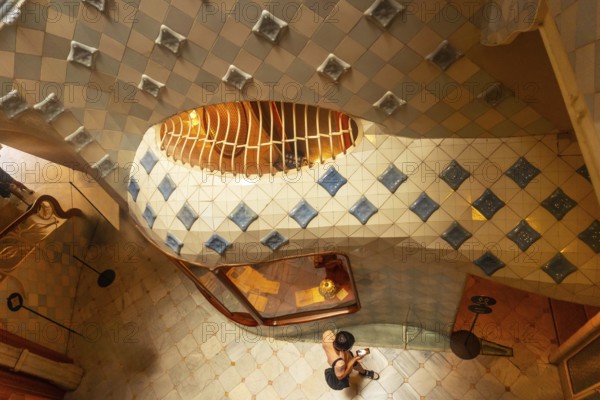 High angle view of a tourist capturing the colorful ceramic tiles and curved staircase design inside casa batllo in barcelona