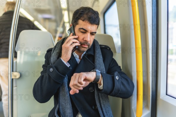 Adult caucasian businessman talking to the mobile phone and checking the time while commuting with metro