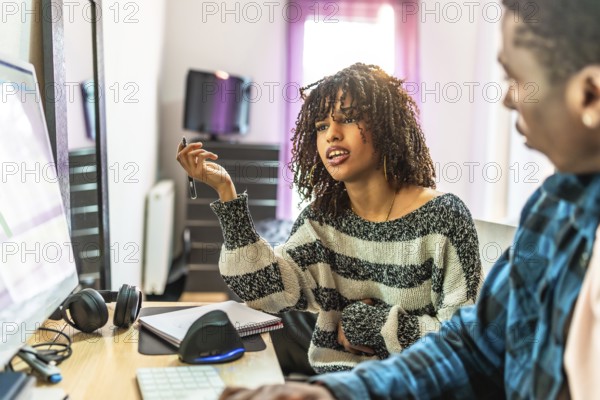 Two web designers collaborating on a project, discussing ideas and solutions while working on a computer in a cozy home office setting