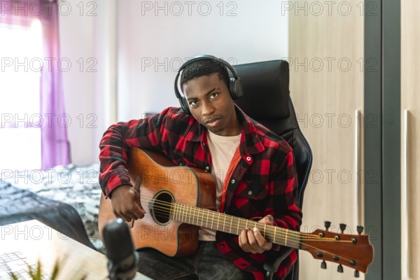 Young man playing acoustic guitar and recording original music in a cozy home studio, immersed in creativity and passion for his art