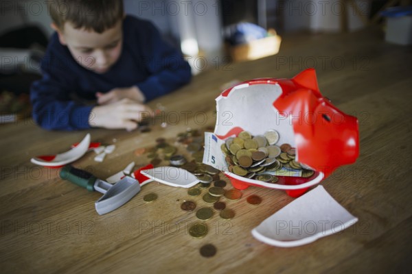 Symbolic photo on the subject of saving. A boy smashes his savings slip and counts the money it contains. Berlin, 10.02.2024