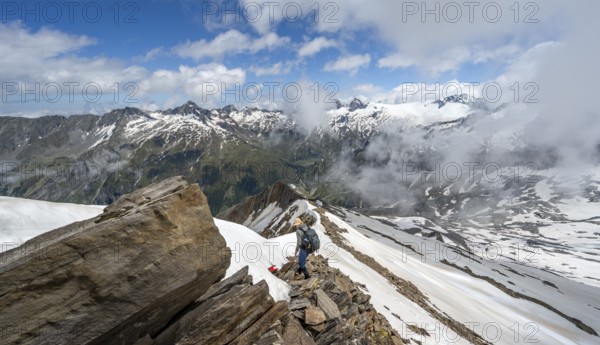 Mountaineer on a rocky ridge with snow, descent from the summit of Schönbichler Horn, view of snow-covered mountain peaks and valley Zemmgrund, Berliner Höhenweg, Zillertal Alps, Tyrol, Austria, Europe