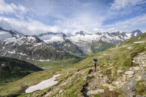 Mountaineer on hiking trail in picturesque mountain landscape, mountain peak with snow and glacier Schwarzensteinkees, Hornkees and Waxeggkees, summit Schwarzenstein, Hornspitzen and Großer Möseler, Berliner Höhenweg, Zillertal Alps, Tyrol, Austria, Europe