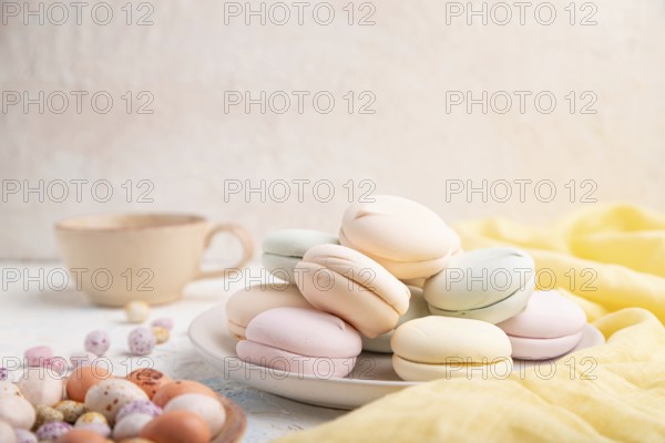 Colored zephyr or marshmallow with cup of coffee and dragees on white concrete background and yellow textile. Side view, copy space, selective focus