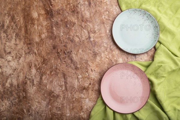 Two empty blue and pink plates on brown concrete background and green textile. Top view, copy space, flat lay