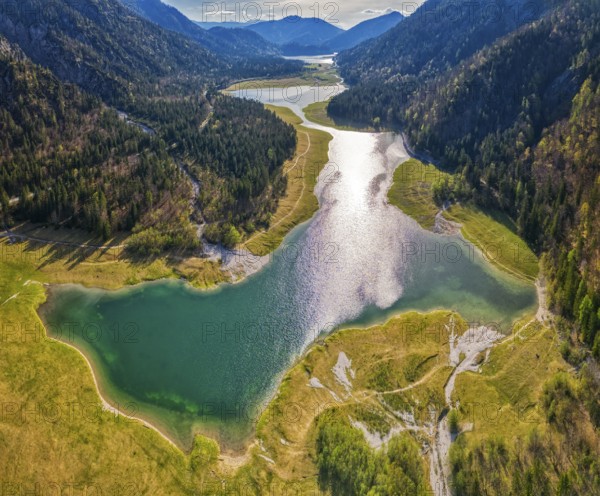 Green mountain landscape with river and lake, sun reflection in the water, surrounded by forests, Mittersee lake