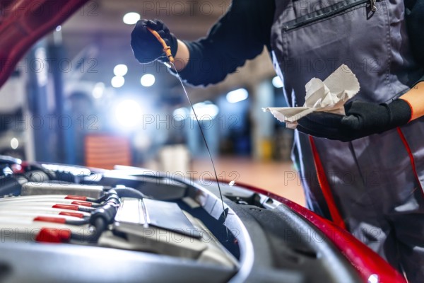 Female car mechanic checking the oil level of a car engine during a maintenance service in a professional workshop