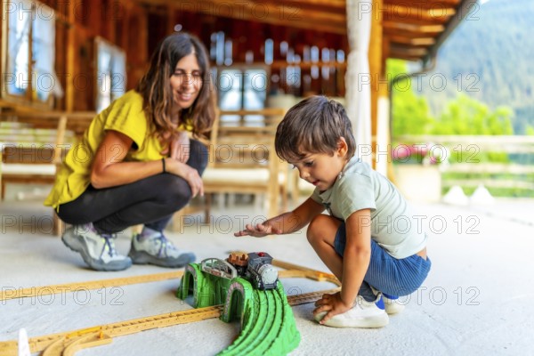 Young boy enjoying a toy train set on a sunny patio with an adult nearby