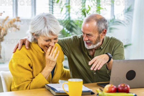 Senior woman looking at household finances notes and expressing surprise and happiness while her husband embracing for the back sitting at home