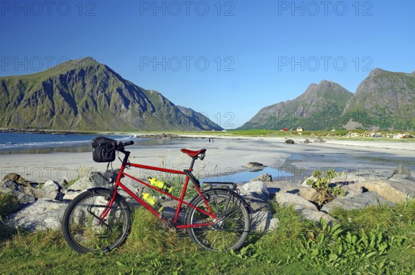 A bicycle on the beach with a view of the surrounding mountains and the sea, Flakstad, Lofoten, Nordland, Norway, Europe