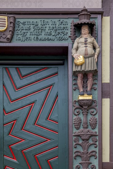 Detailed wooden door of a half-timbered house with statue and decorated façade, clear zigzag pattern, lettering and coat of arms, Wernigerode, Harz, Saxony-Anhalt, Germany, Europe