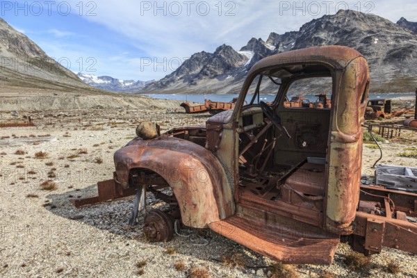 Rusted car and oil drums in front of steep mountains, remains of a US airbase from the Second World War, Ikateq Fjord, East Greenland, Greenland, North America