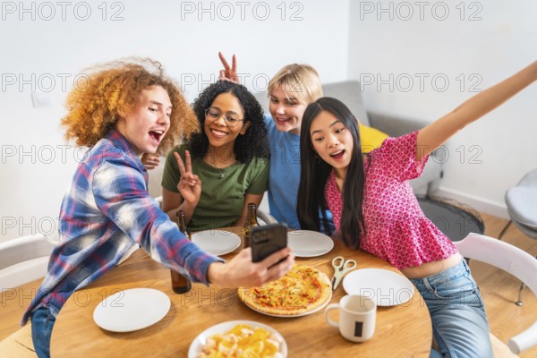Four diverse friends capture a fun moment with a selfie while having pizza, snacks, and drinks at a casual get together