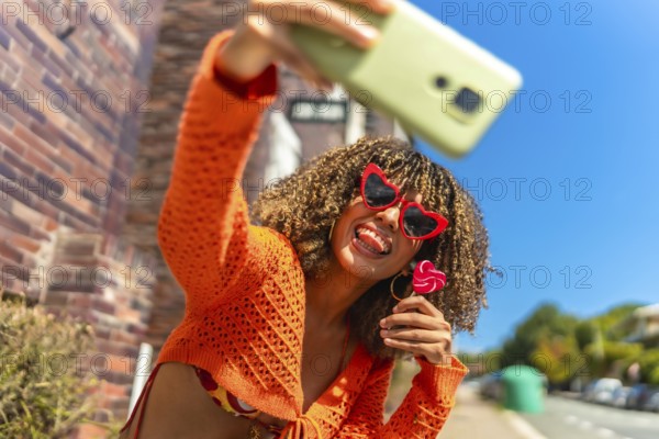 Young and vital latin woman taking selfie while eating lollipop outdoors