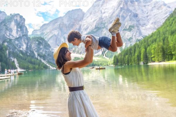 Happy mother lifting her son, enjoying summer vacation at lake braies - pragser wildsee - in the dolomites mountains, south tyrol, alps, italy