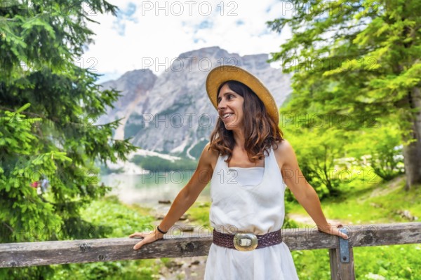 Woman wearing straw hat enjoying the landscape at lake braies, also called pragser wildsee, during summer vacation in the dolomites