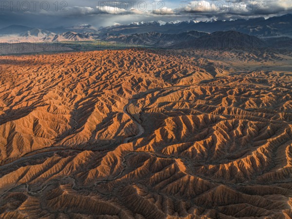Landscape of eroded hills, badlands at sunset, mountain peaks of the Tian Shan Mountains in the background, aerial view, Canyon of the Forgotten Rivers, Issyk Kul, Kyrgyzstan, Asia