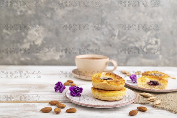 Small cheesecakes with jam and almonds with cup of coffee on a white wooden background and linen textile. Side view, copy space