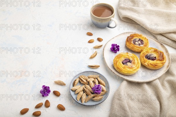 Small cheesecakes with jam and almonds with cup of coffee on a white concrete background and linen textile. Side view, copy space