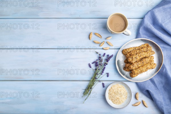 Crumble cookies with seasme and almonds on ceramic plate with cup of coffee and blue linen textile on blue wooden background. top view, flat lay, copy space