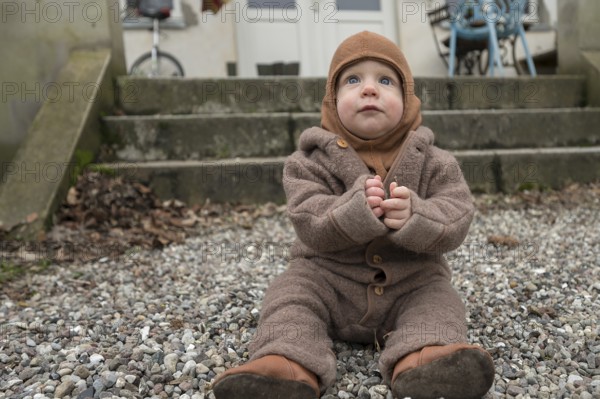Small child, 8 months, wrapped up warm, sitting on the gravel and playing with stones, Mecklenburg-Vorpommern, Germany, Europe