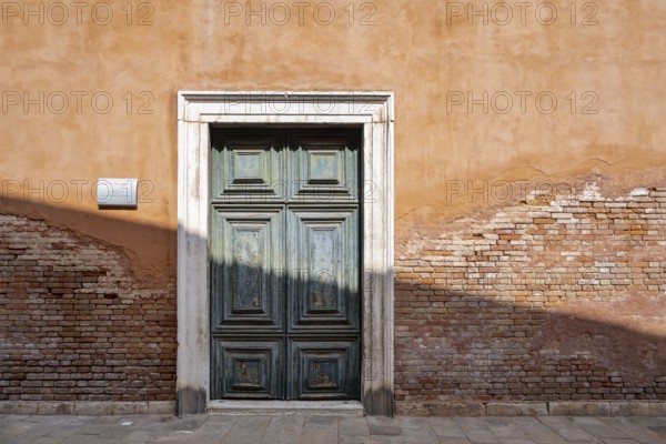 Red house facade with large green door, peeling plaster on brick wall, Venice, Veneto, Italy, Europe