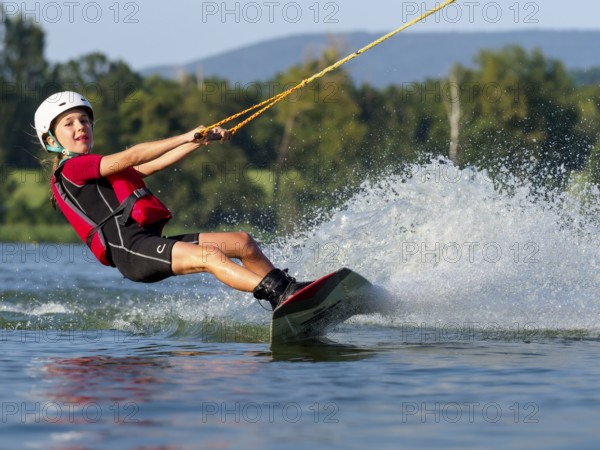 Boy or girl, water sports and fast ride with wakeboard, red life jacket, water skiing in the wake park