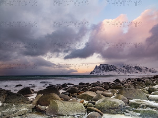 Rounded rocks on Utakleiv beach in a dramatic cloudy atmosphere, snow-capped mountains in the background, Vestvagoy Island, Lofoten, Norway, Europe