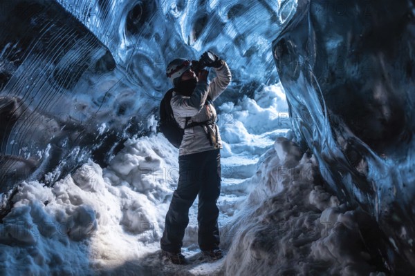 A woman is standing in a cave with snow on the ground. She is wearing a backpack and a white jacket