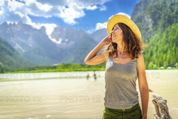 Tourist wearing a straw hat enjoying the stunning view of the dolomites reflected in the serene waters of lago di landro