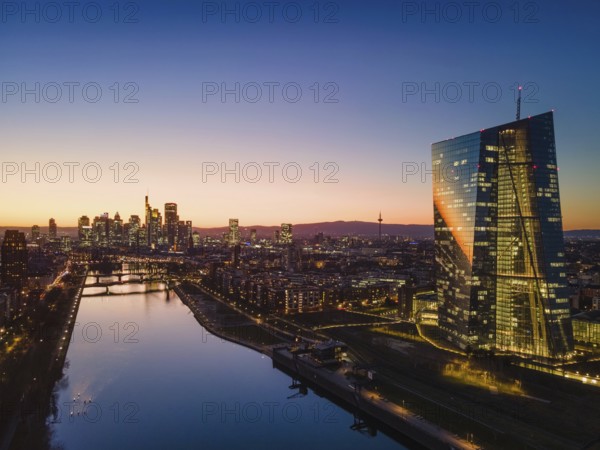 The lights in the offices of the European Central Bank (ECB) and the Frankfurt skyline glow in the evening after sunset. (Aerial view with a drone), Osthafen, Frankfurt am Main, Hesse, Germany, Europe